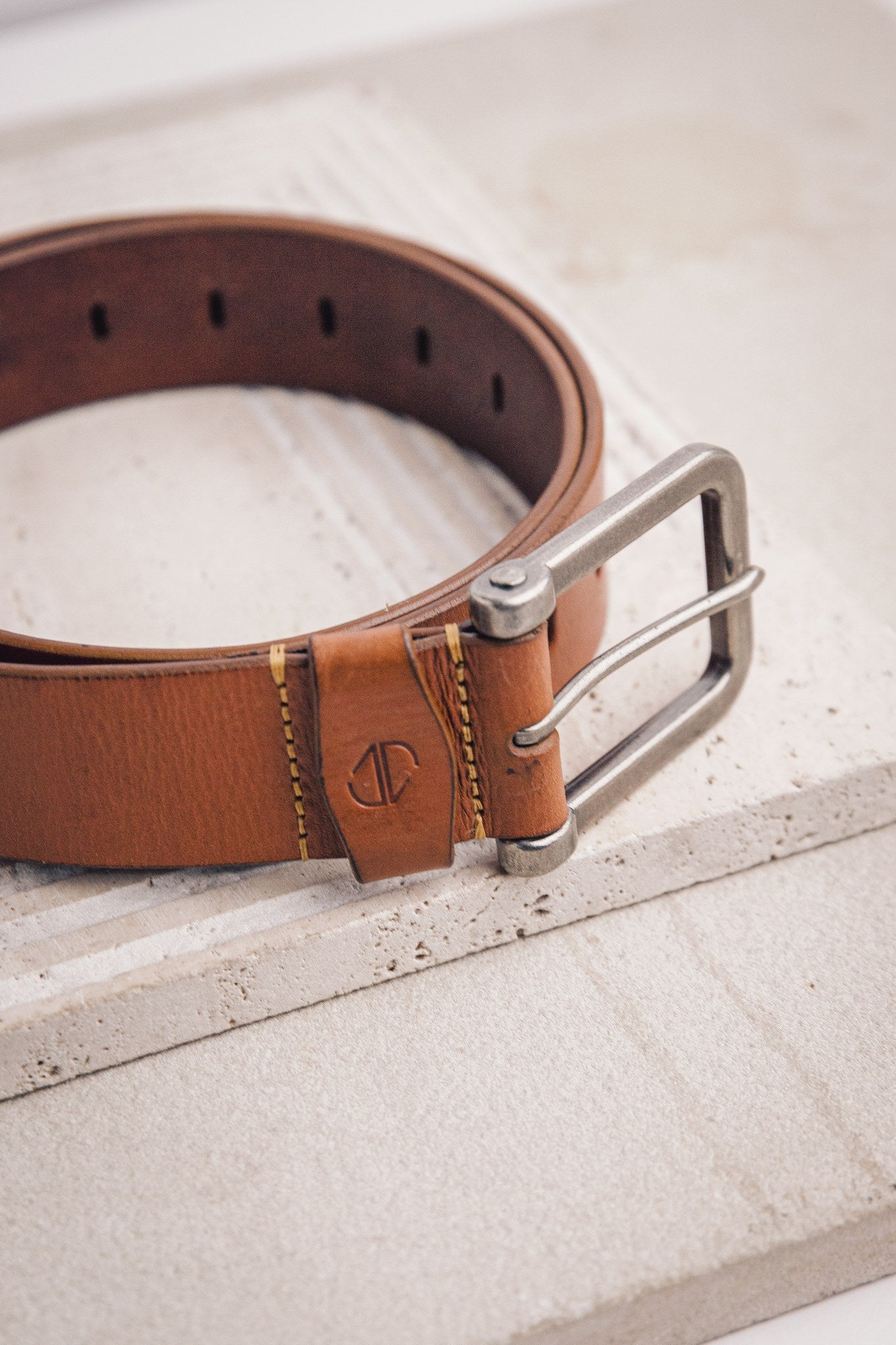 The Alarico belt in tan milled leather, composed and at rest