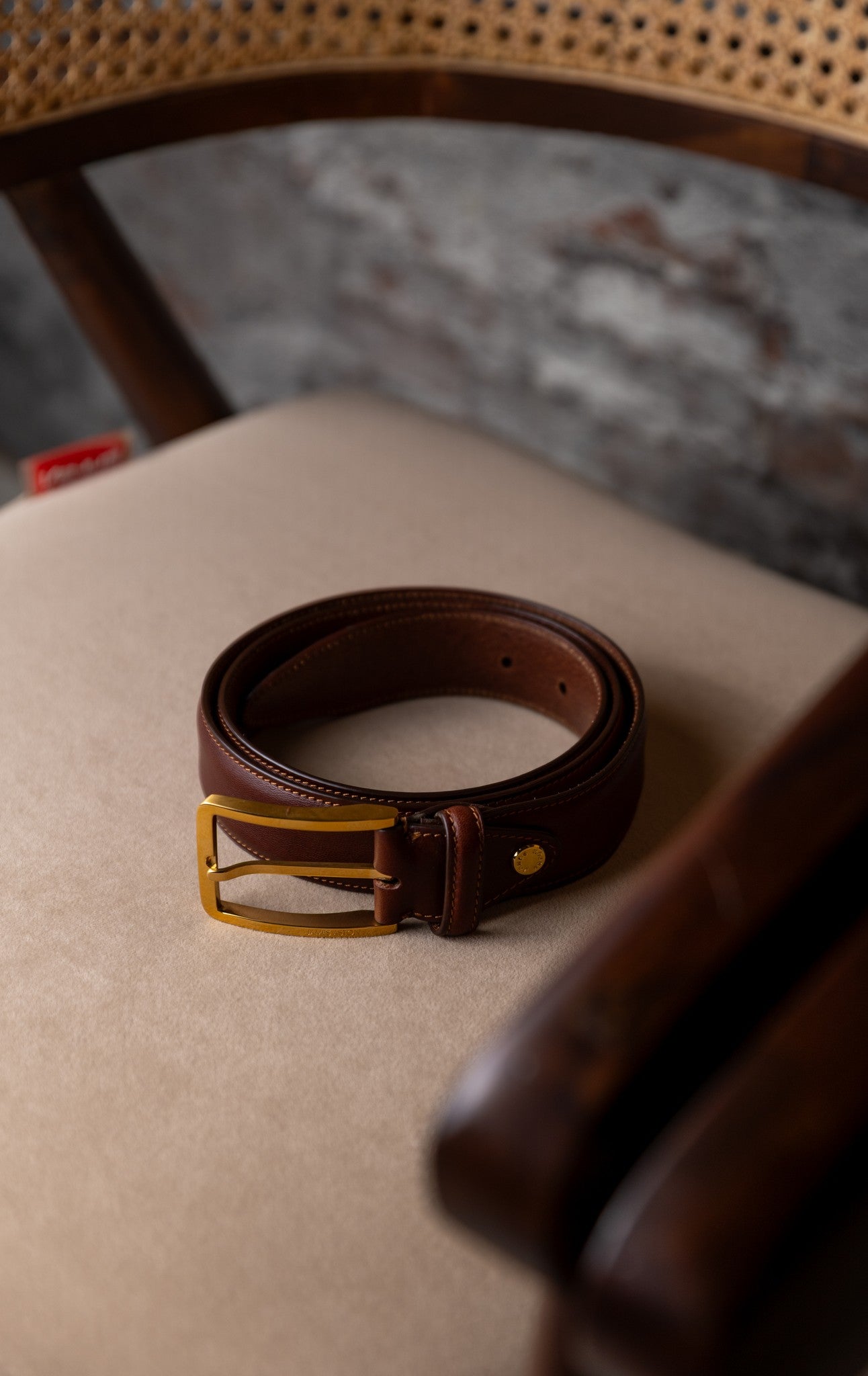 The Raffaello oak brown milled Vachetta leather belt resting on a kraft box, showing the gold buckle